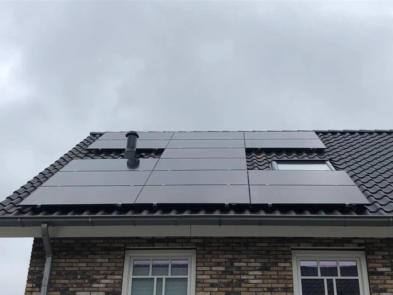 Full-black zonnepanelen op een woonhuis rond dakramen en een rookgasdoorvoer